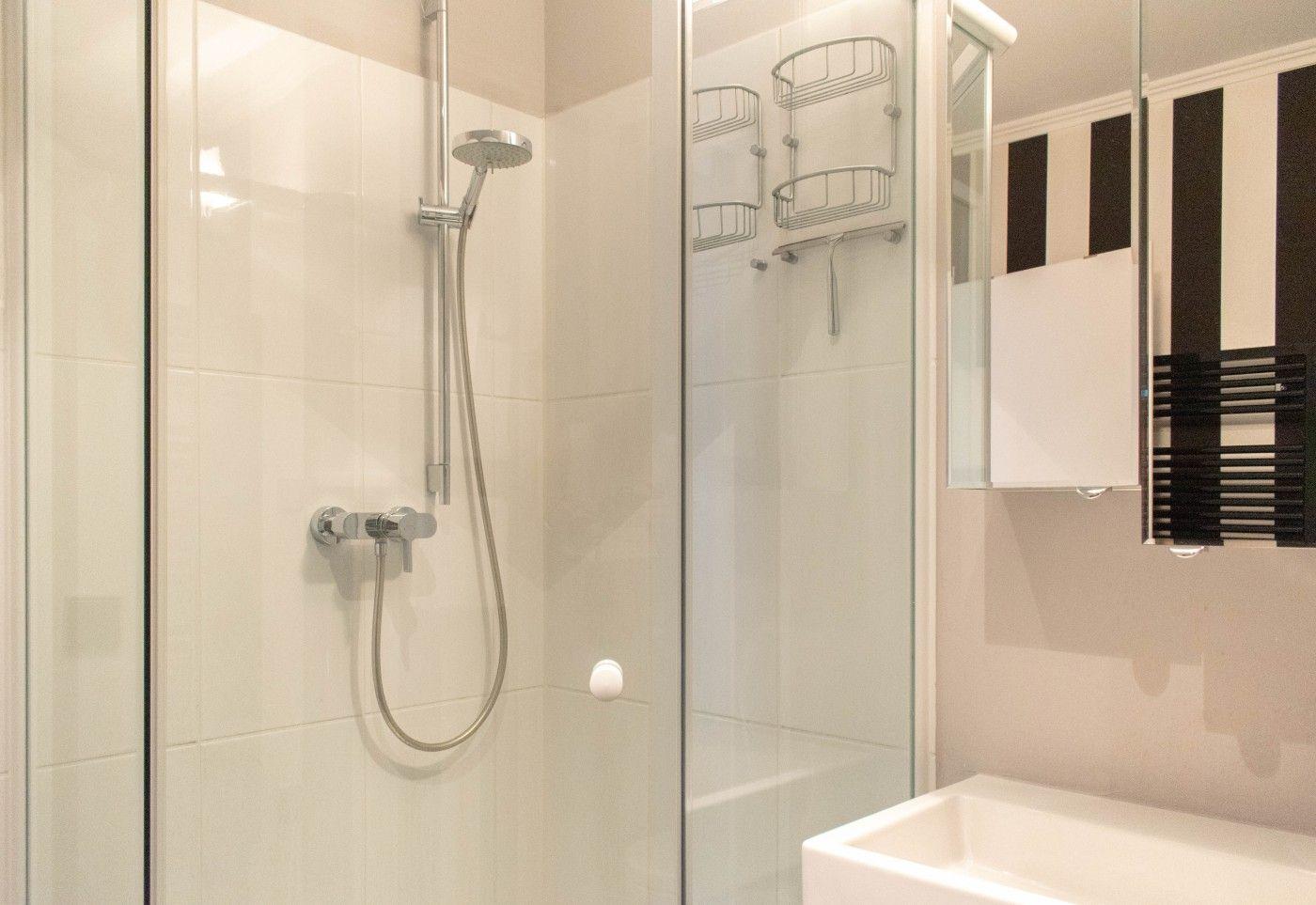 Dusche mit Duschbrause und Handbrause, Spiegel und Waschbecken im Badezimmer.