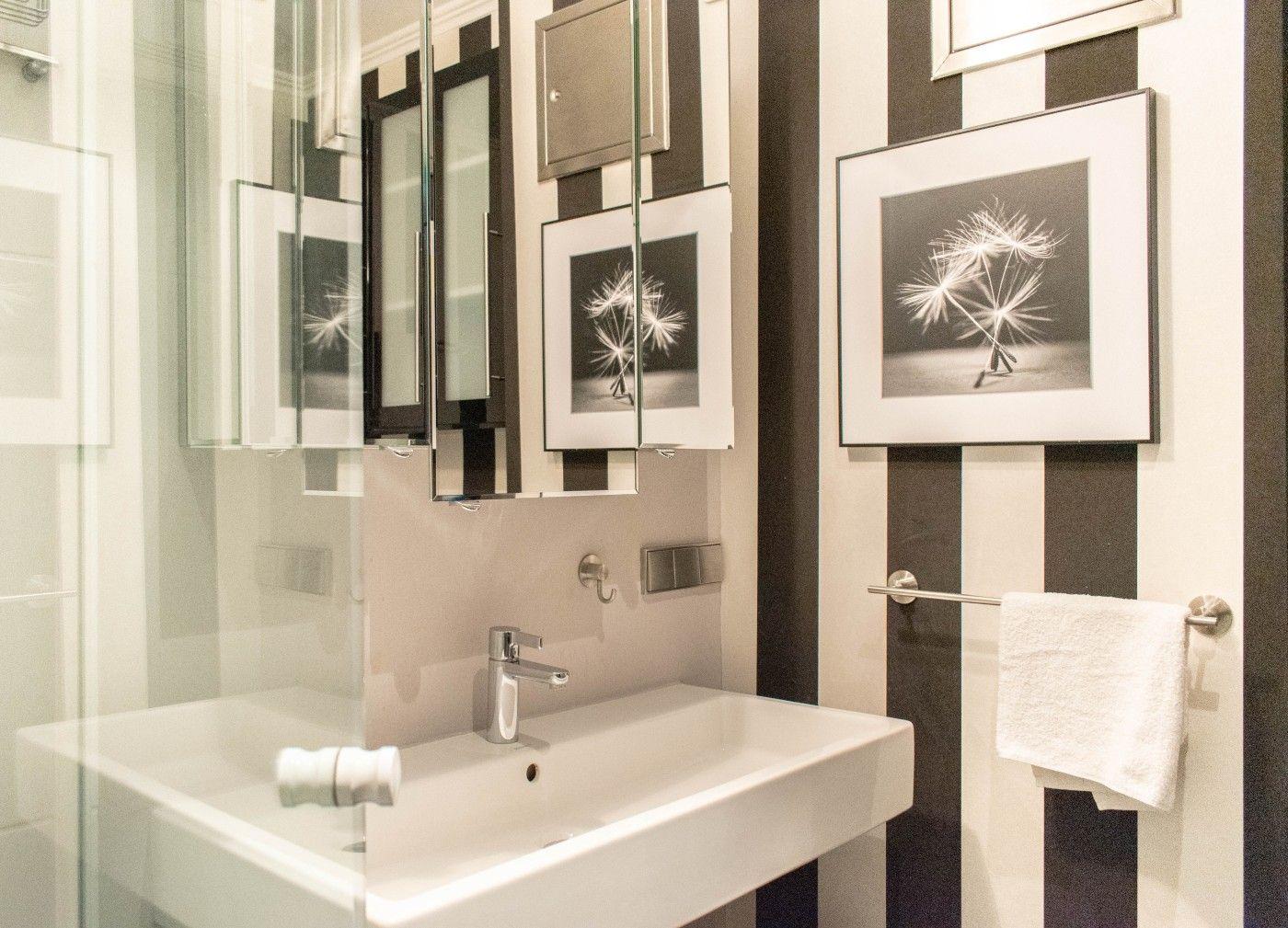 Badezimmer mit Waschbecken, Spiegel und Wandbildern an schwarz-weißen Streifen.