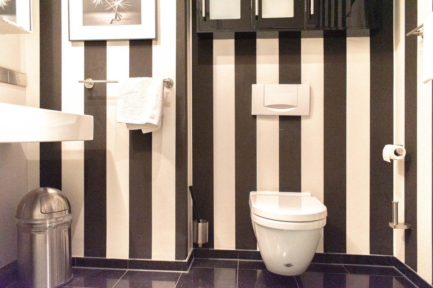 Badezimmer mit schwarz-weißen Streifen, Toilette, Waschbecken und Spiegel.