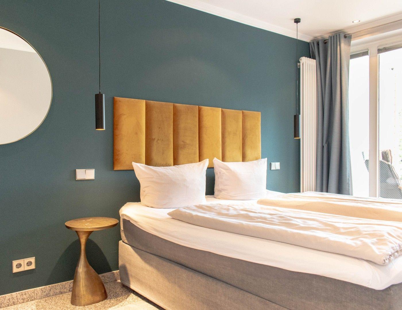 Schlafzimmer mit Bett, Kopfteil, Wandspiegel und Fenster