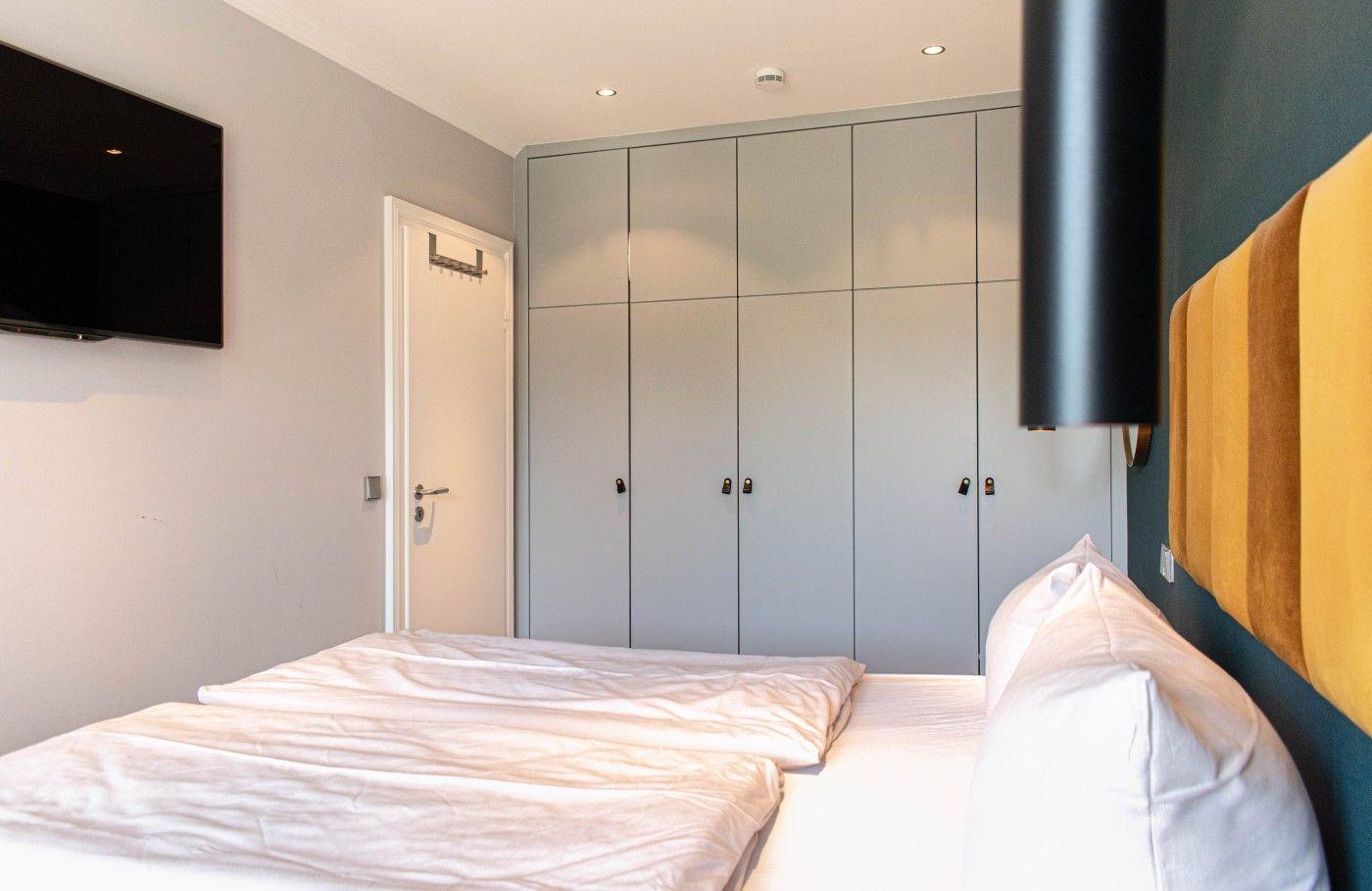 Schlafzimmer mit Doppelbett, Kleiderschrank und Wandfernseher.