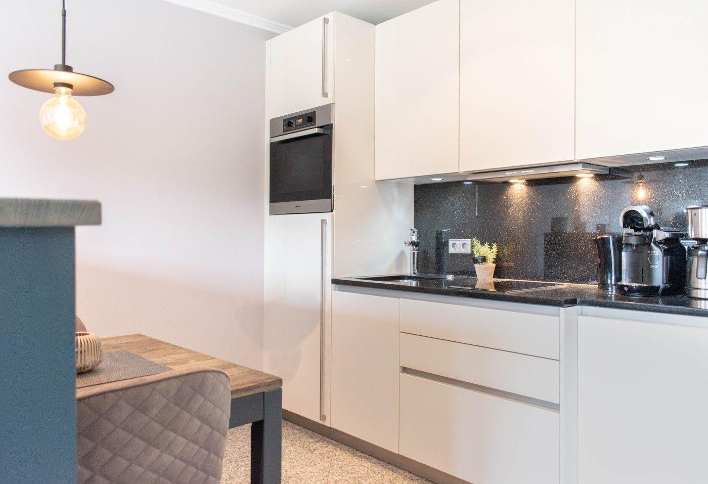 Küche mit weißen Schränken, schwarzer Arbeitsplatte und integriertem Ofen.