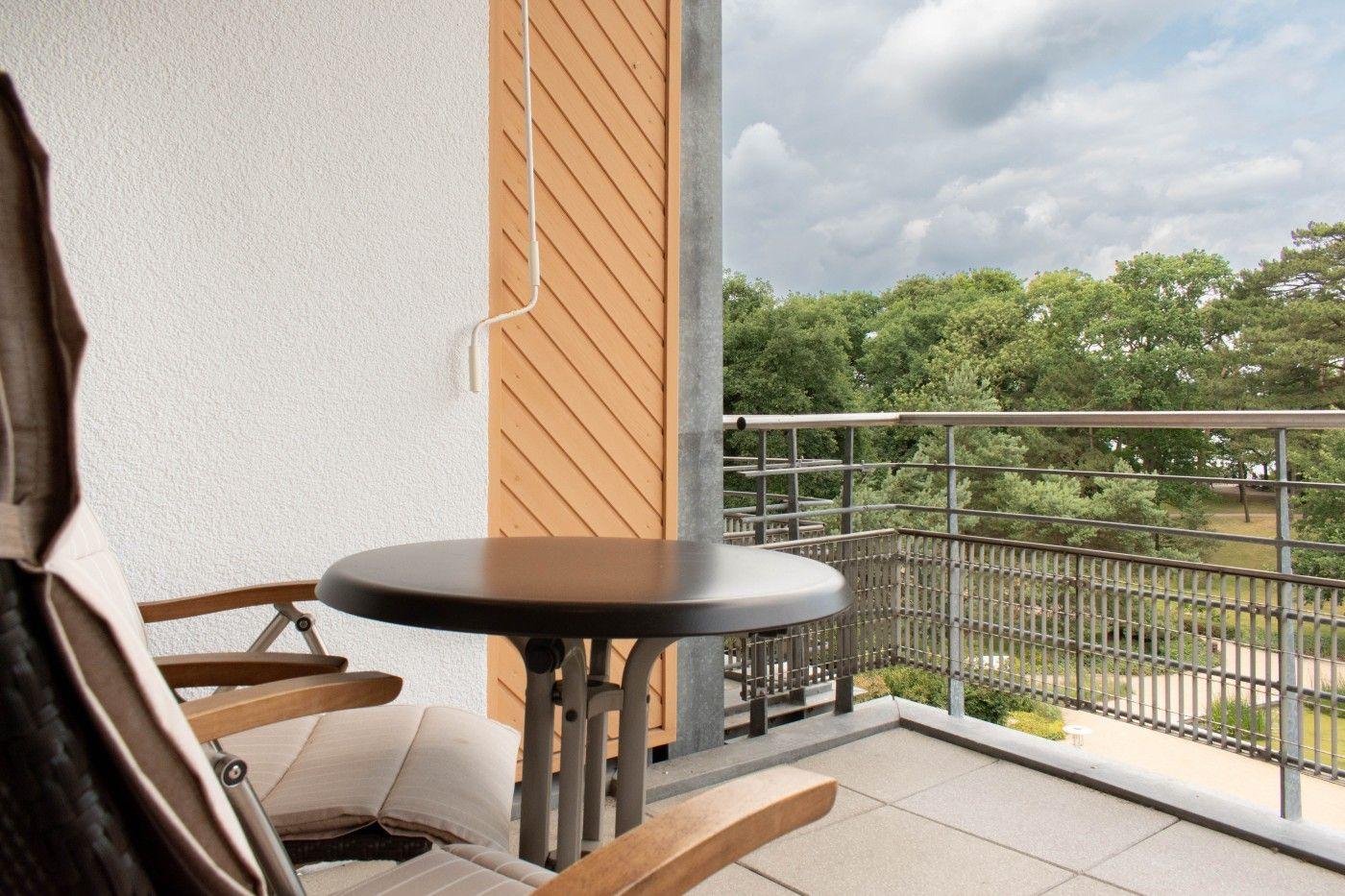 Terrasse mit Tisch und Stuhl, Blick auf grüne Bäume und Himmel.