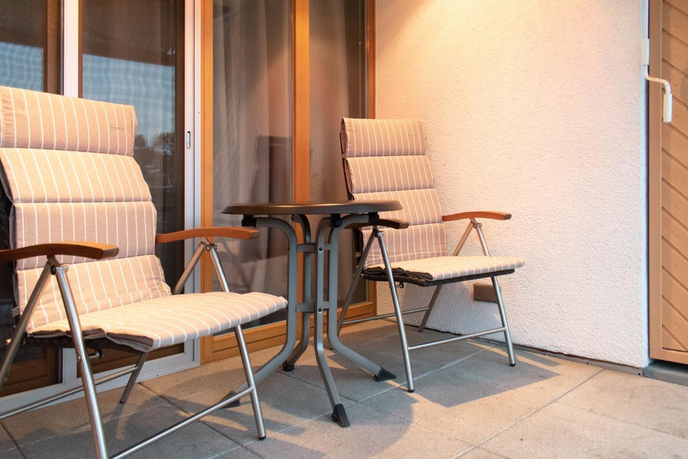 Terrasse mit zwei Sesseln und Tisch. Hintergrund: Glas-Tür und Wand.