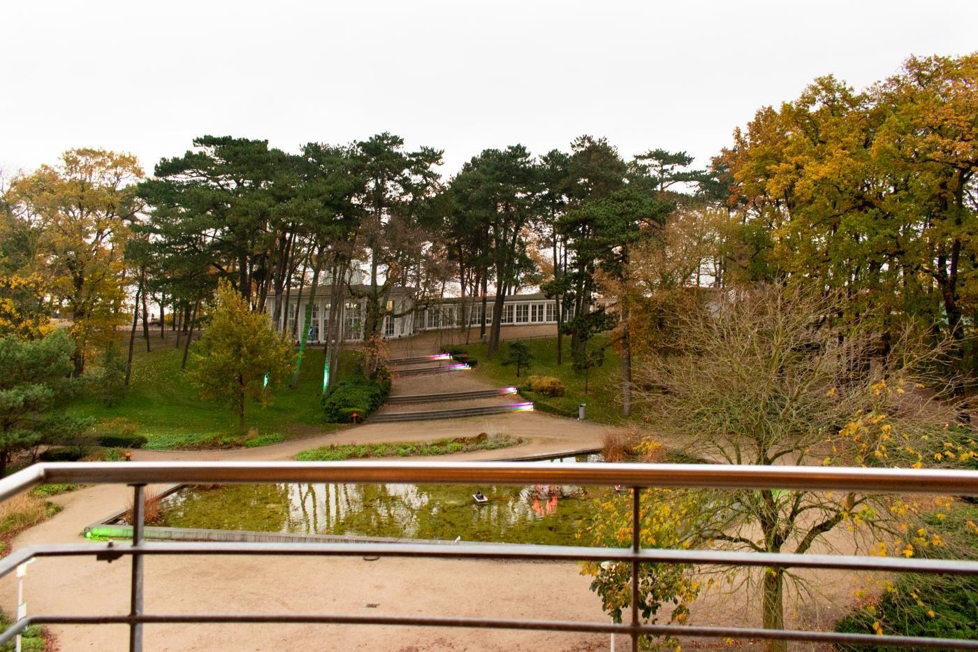 Vom Balkon aus Blick auf einen Teich, einen Weg und ein Gebäude im Wald.