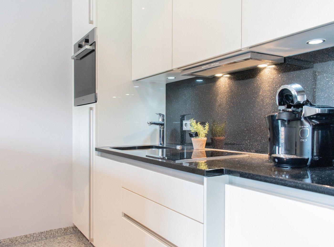 Moderne Küche mit weißen Schränken, schwarzer Arbeitsplatte und Edelstahlgeräten.