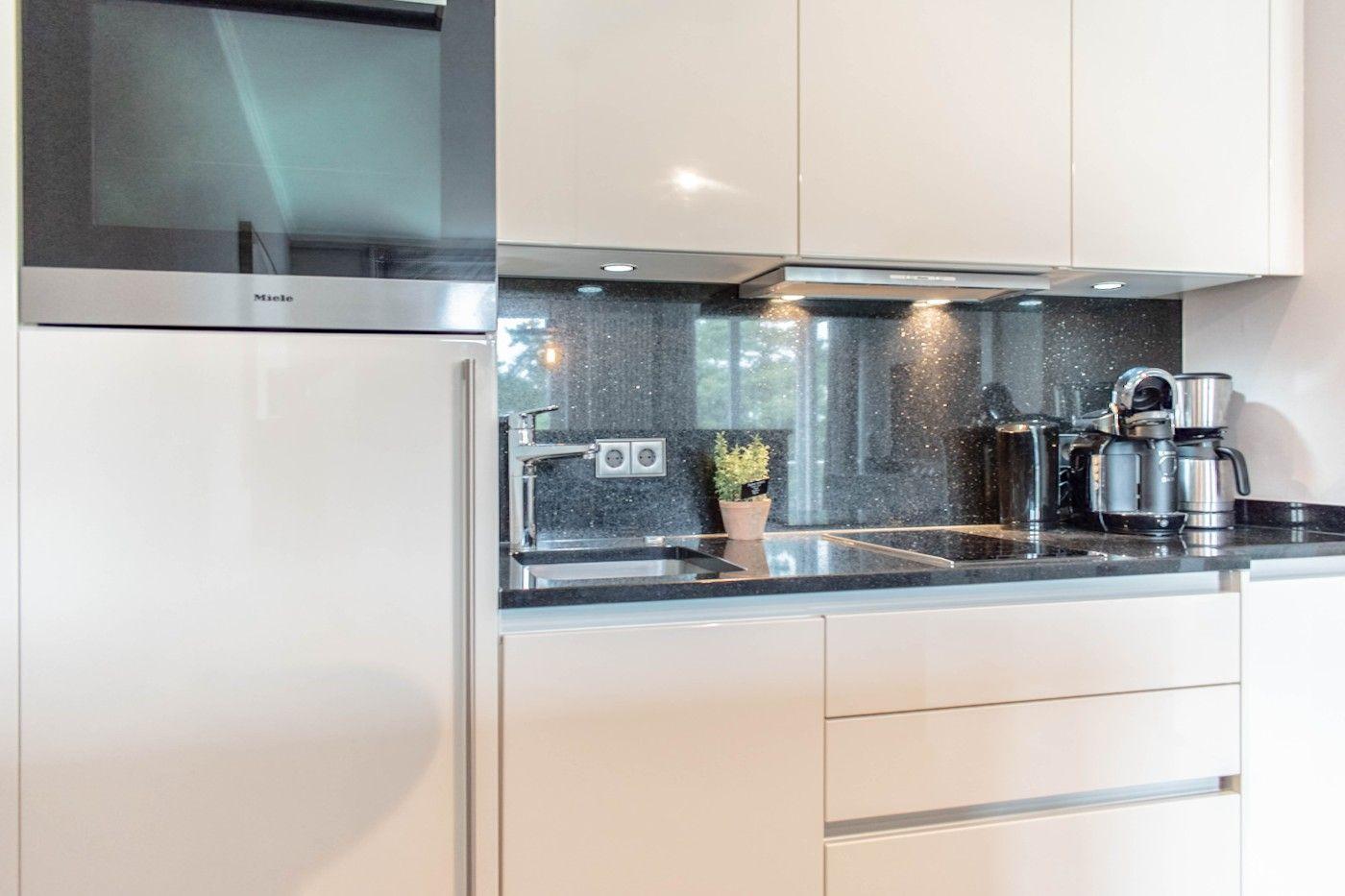 Moderne Küche mit Edelstahlspüle, dunkler Arbeitsplatte und integriertem Kühlschrank.