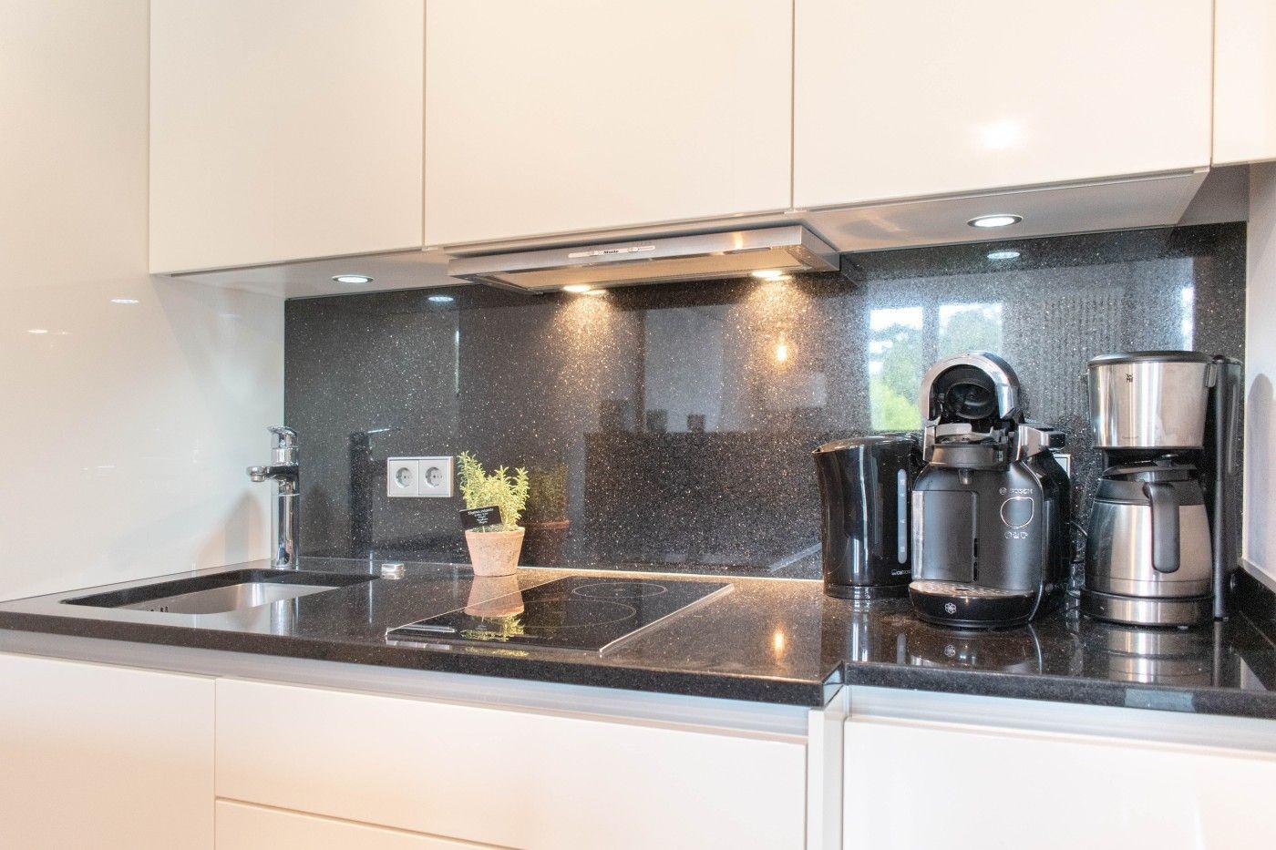 Moderne Küche mit schwarzer Arbeitsplatte und weißen Schränken. Darauf stehen Küchengeräte und eine Pflanze.