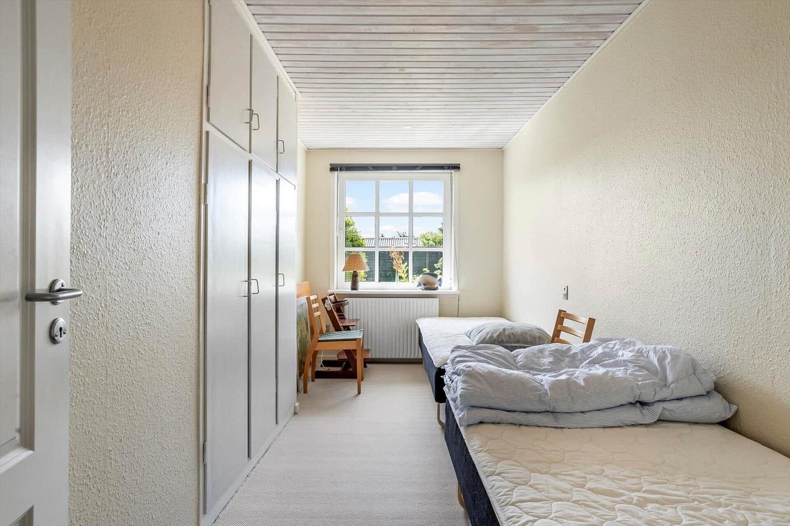 Bedroom with two beds, wardrobe, and window with view outside.