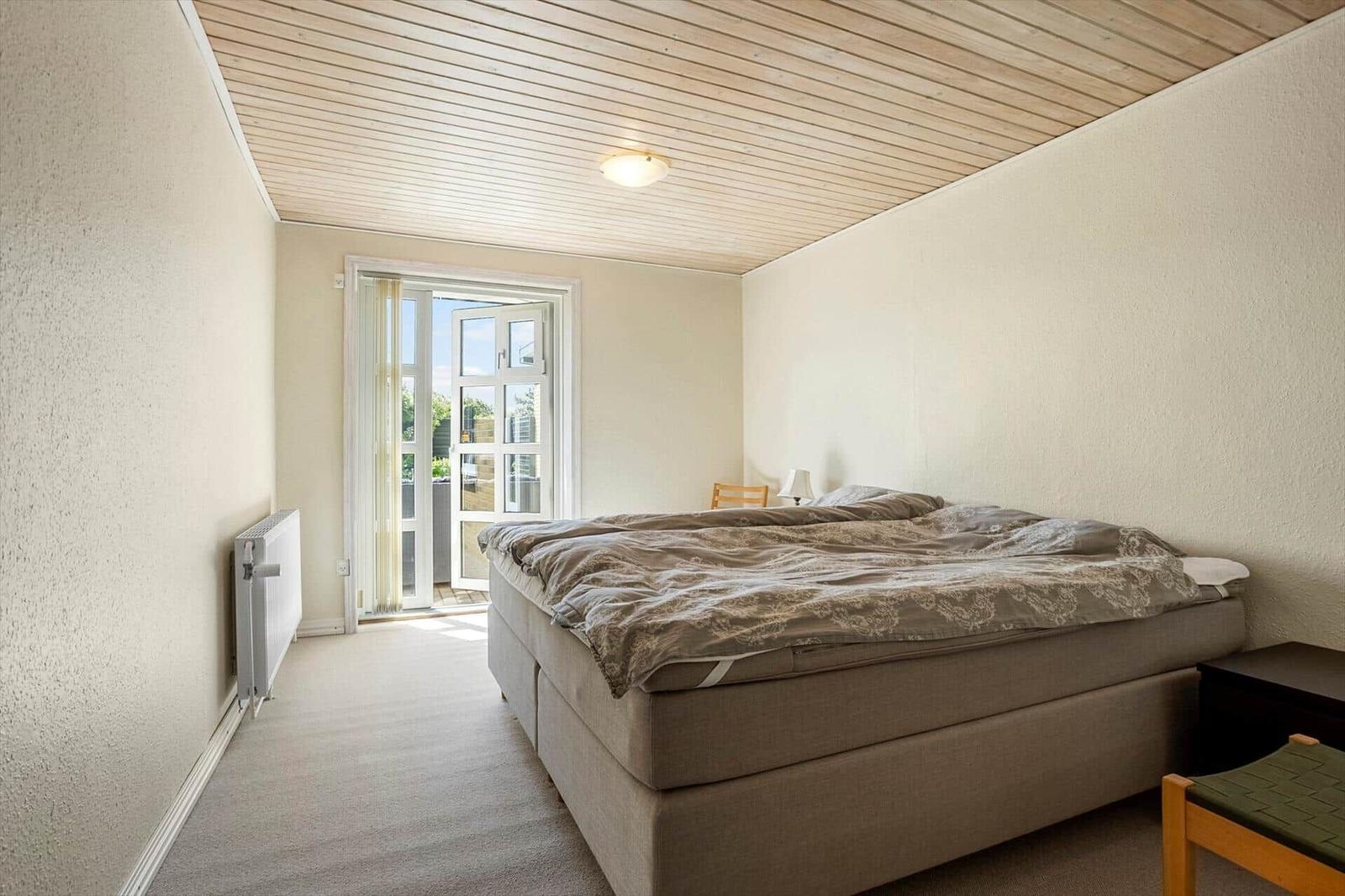 Bedroom with bed, door to balcony, and wooden ceiling.