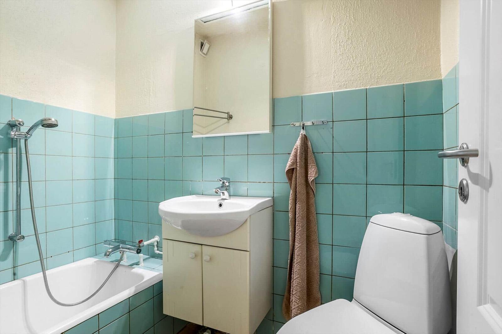 Bathroom with bathtub, mirror cabinet, and toilet. Walls tiled in turquoise.