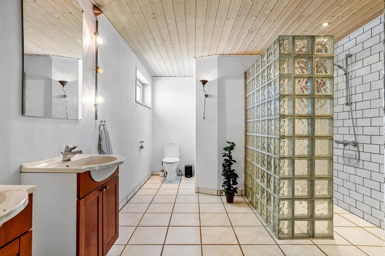 Bathroom with shower, toilet, and sink. Glass block wall and wooden ceiling.