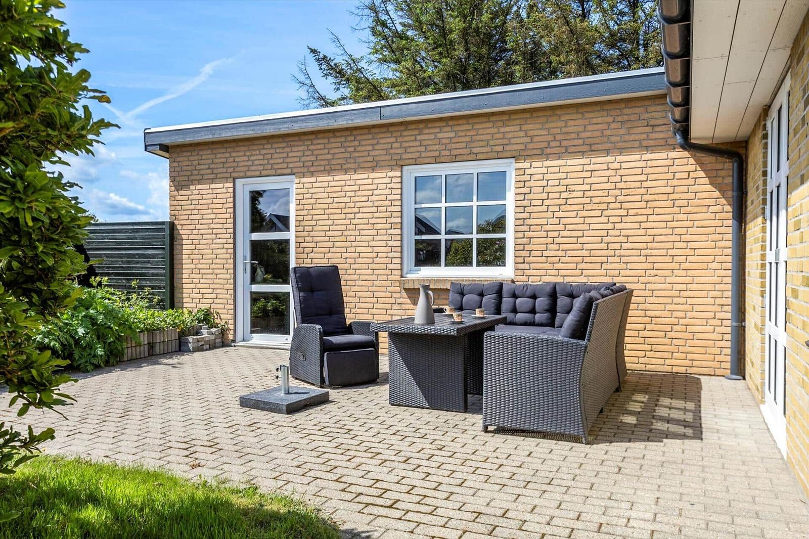 Terrace with seating group, recliner, and table in front of a brick house.