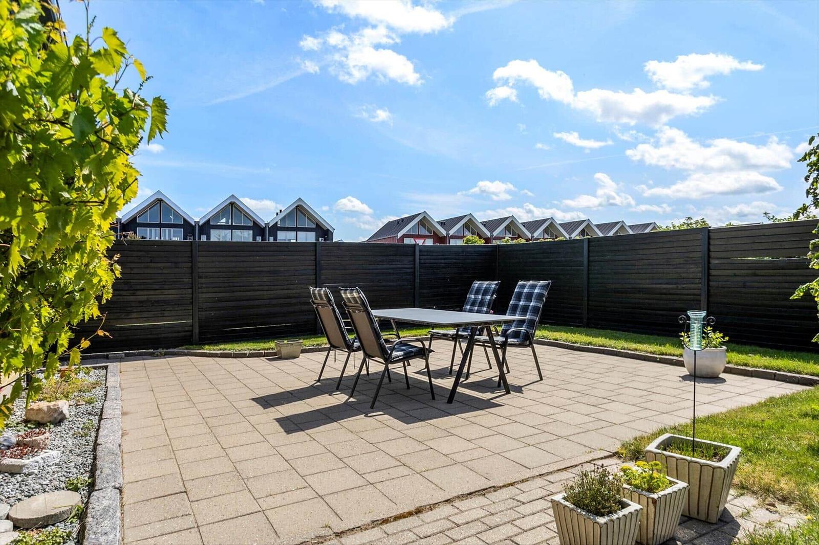 Terrace with table and chairs, surrounded by greenery and fence.