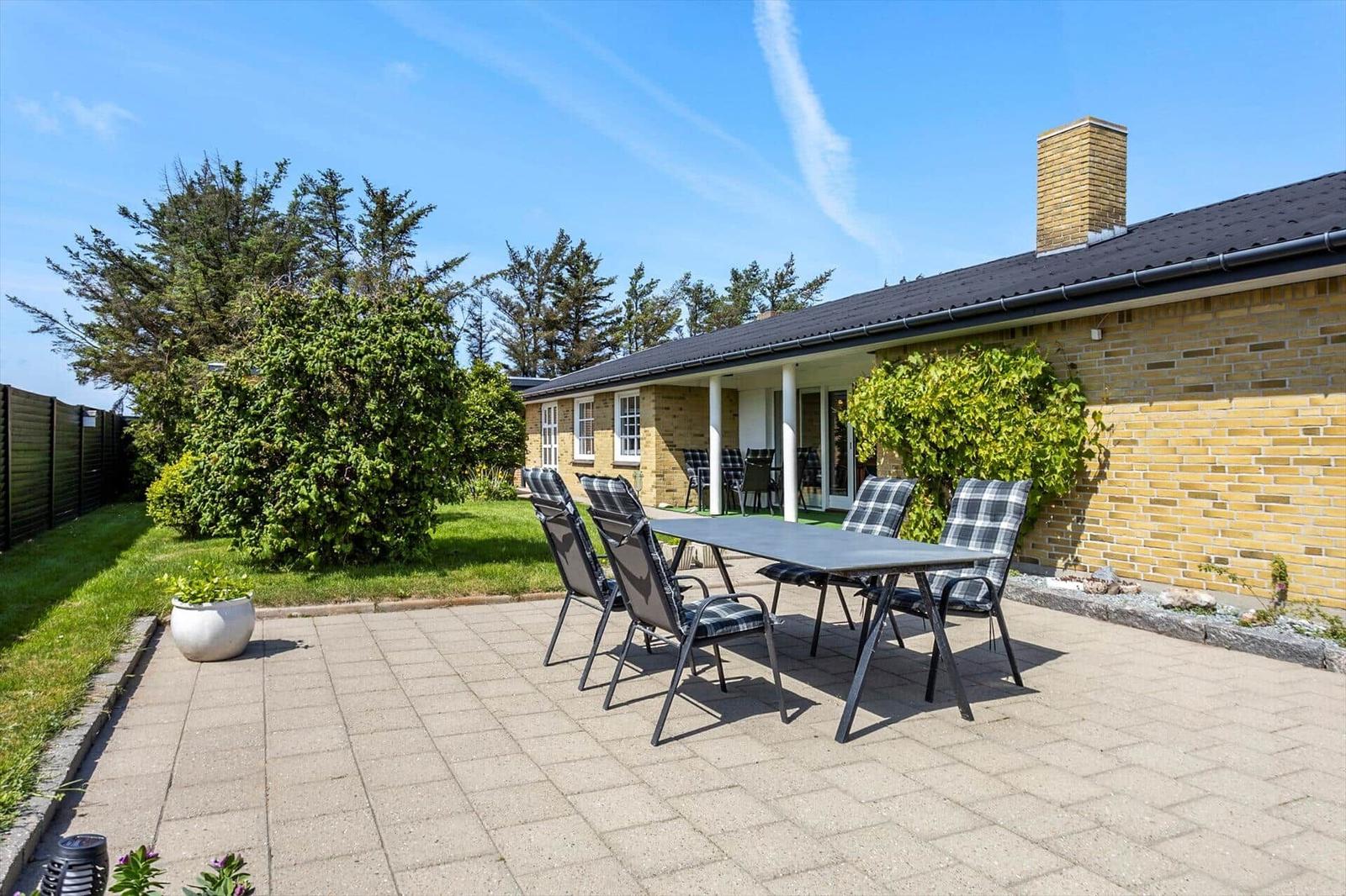 Terrace with table and chairs in front of a house with garden.