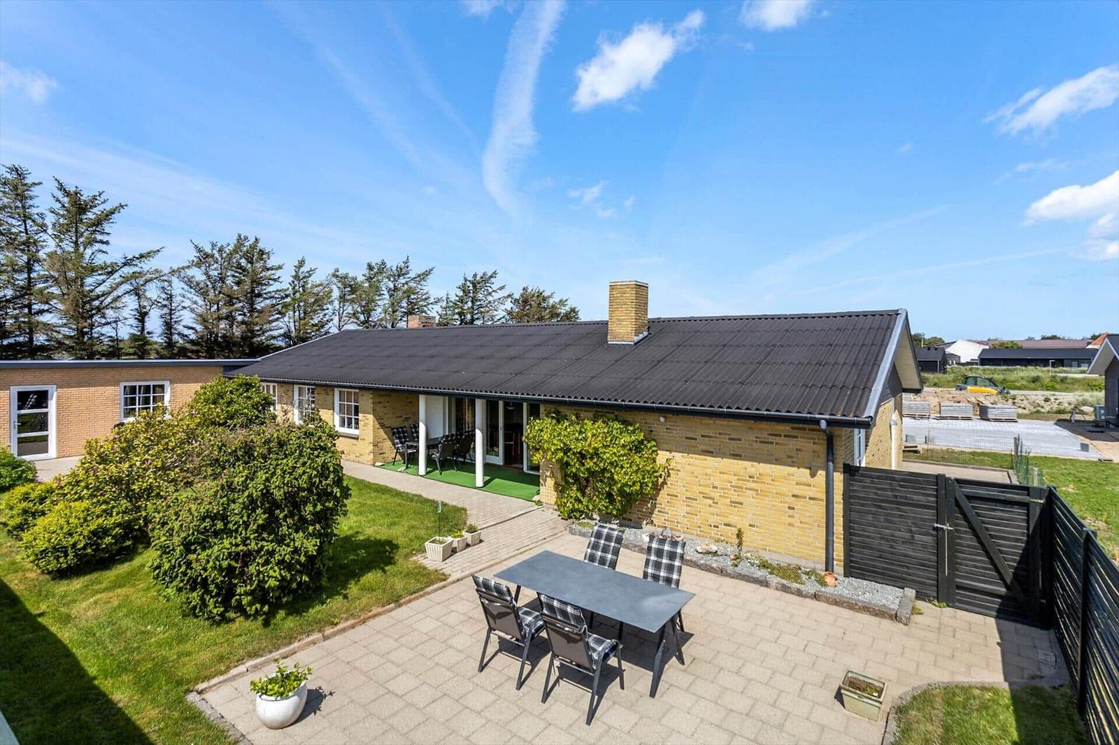 A house with terrace, garden, and table with chairs under blue sky.
