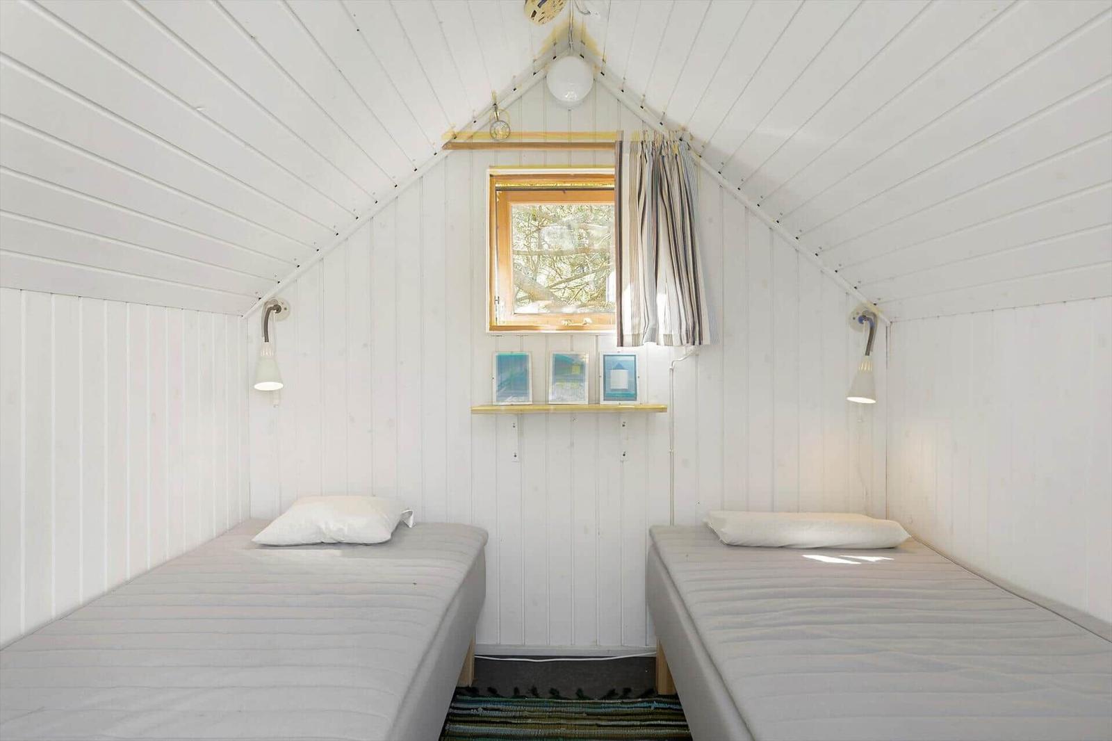 Two single beds in a room with white wood paneling and a window.