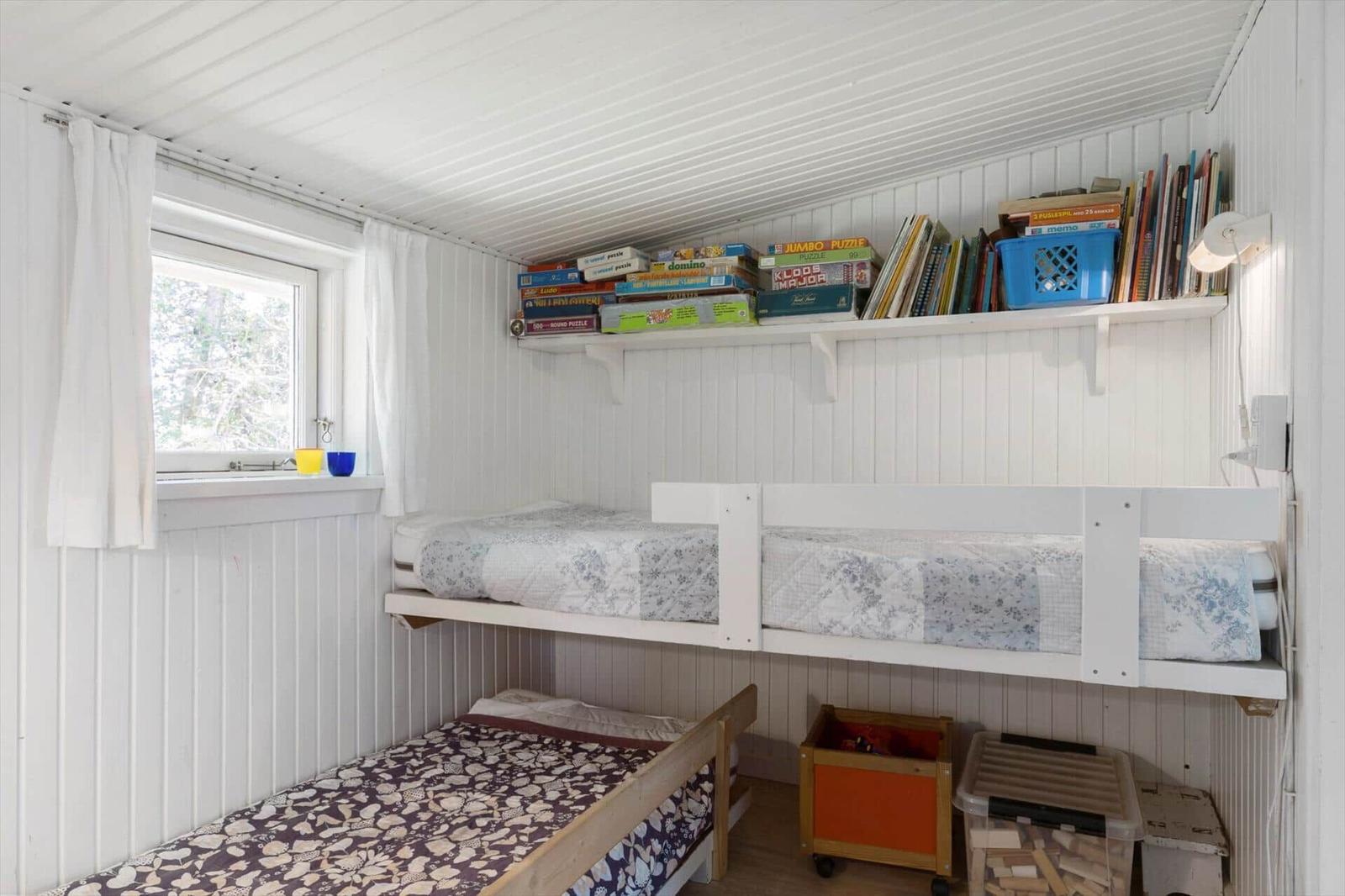 Room with bunk bed, lower bed, and shelf with books and games.
