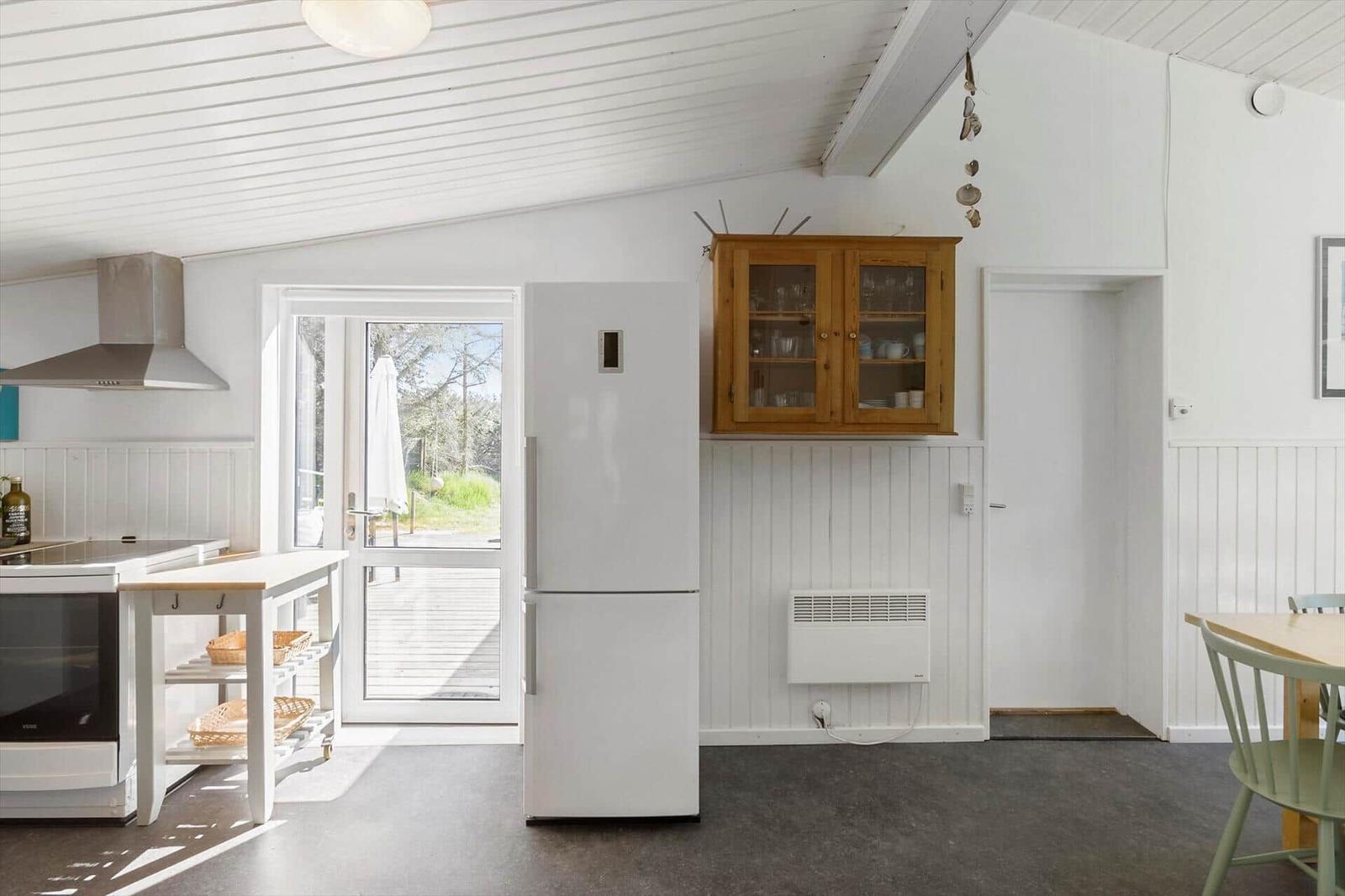 Kitchen with refrigerator, wooden cabinets, and table. Passage to the terrace.