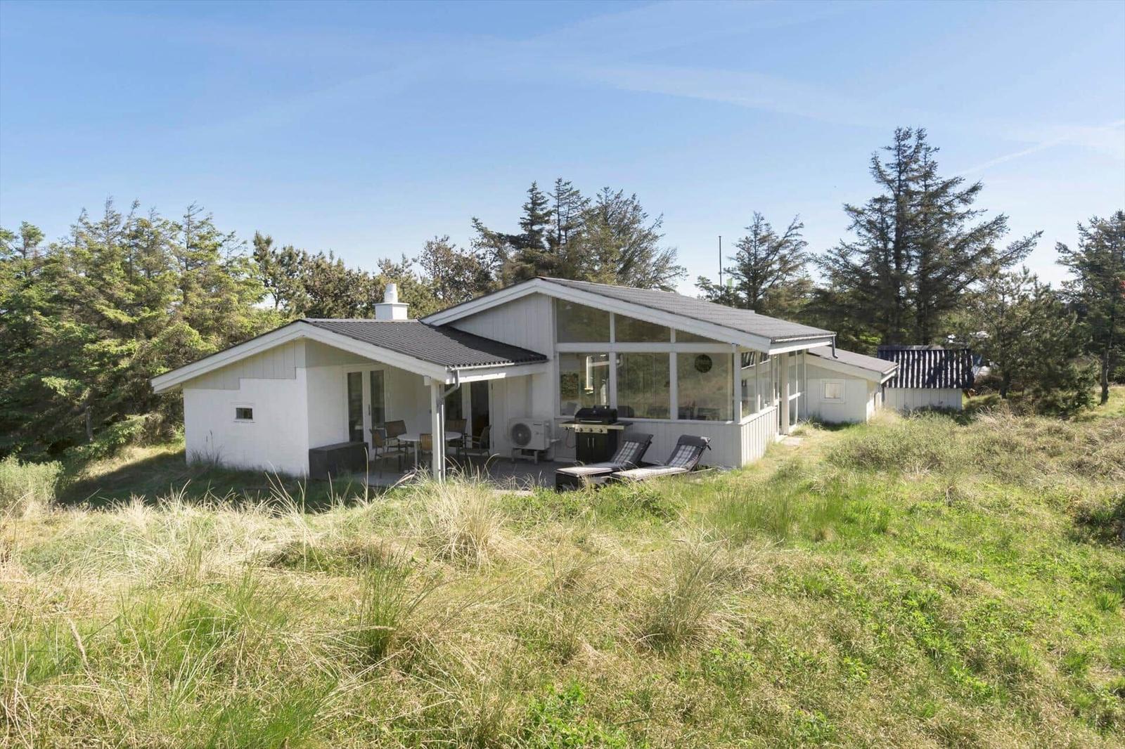 White vacation house with terrace, grill, and loungers in grassland.