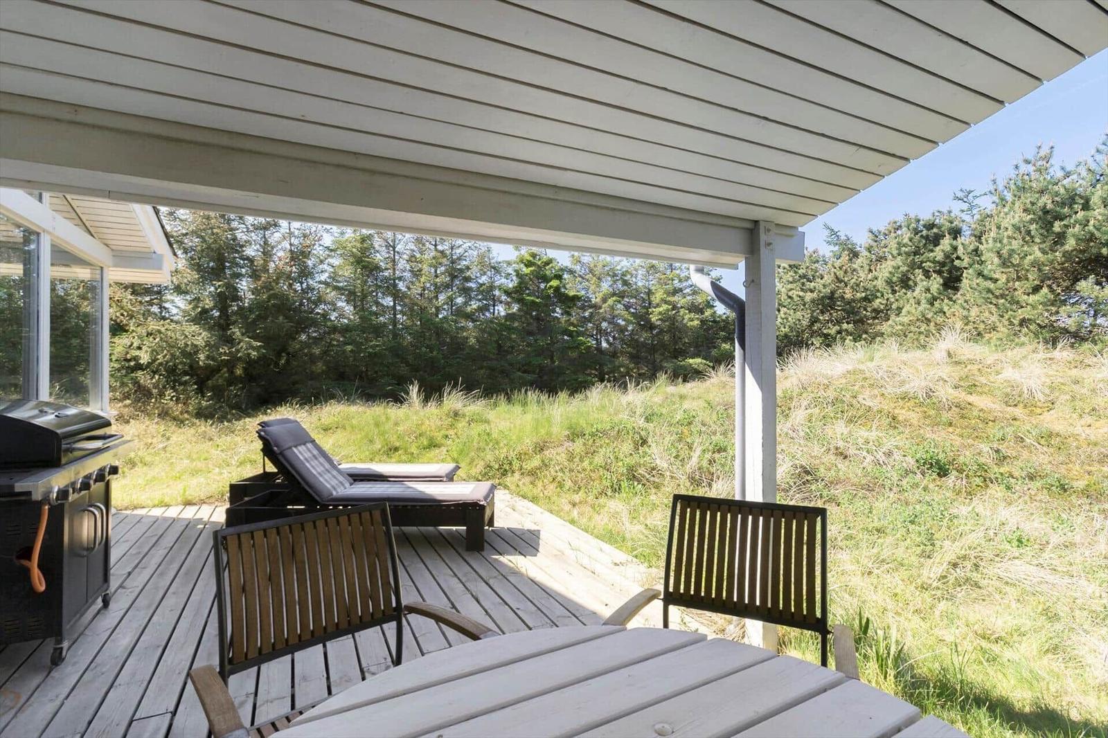 Deck with grill, lounge chair, and table. View of grassy slope and forest.
