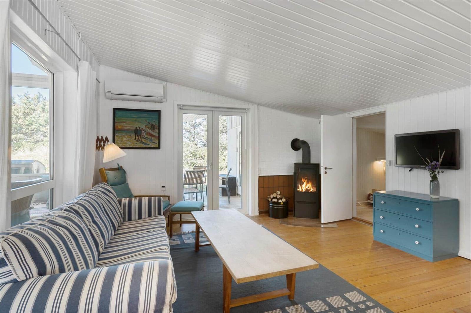 Living room with sofa, fireplace, and TV. Wooden floor and large windows.