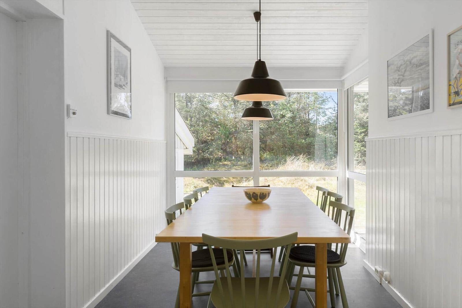 Dining room with wooden table, chairs, and large windows. Ceiling with wood paneling and pendant lamp.