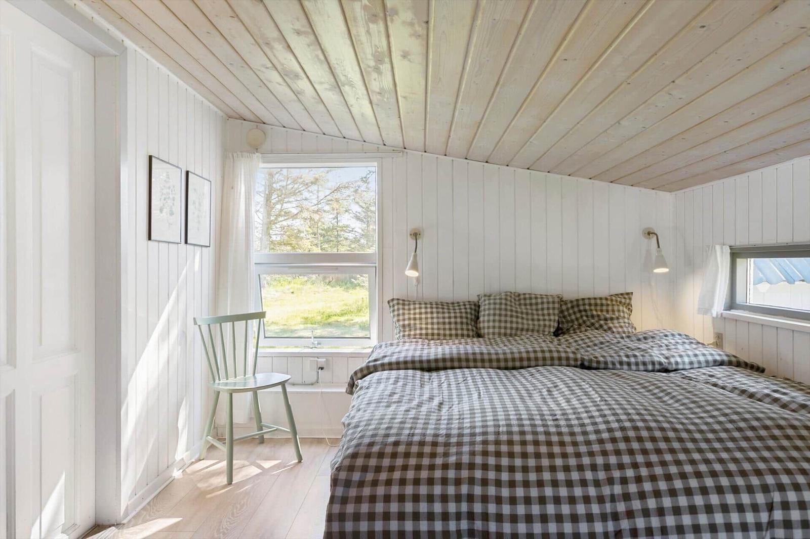 Bedroom with bed, window, and chair. Wooden ceiling and white walls.