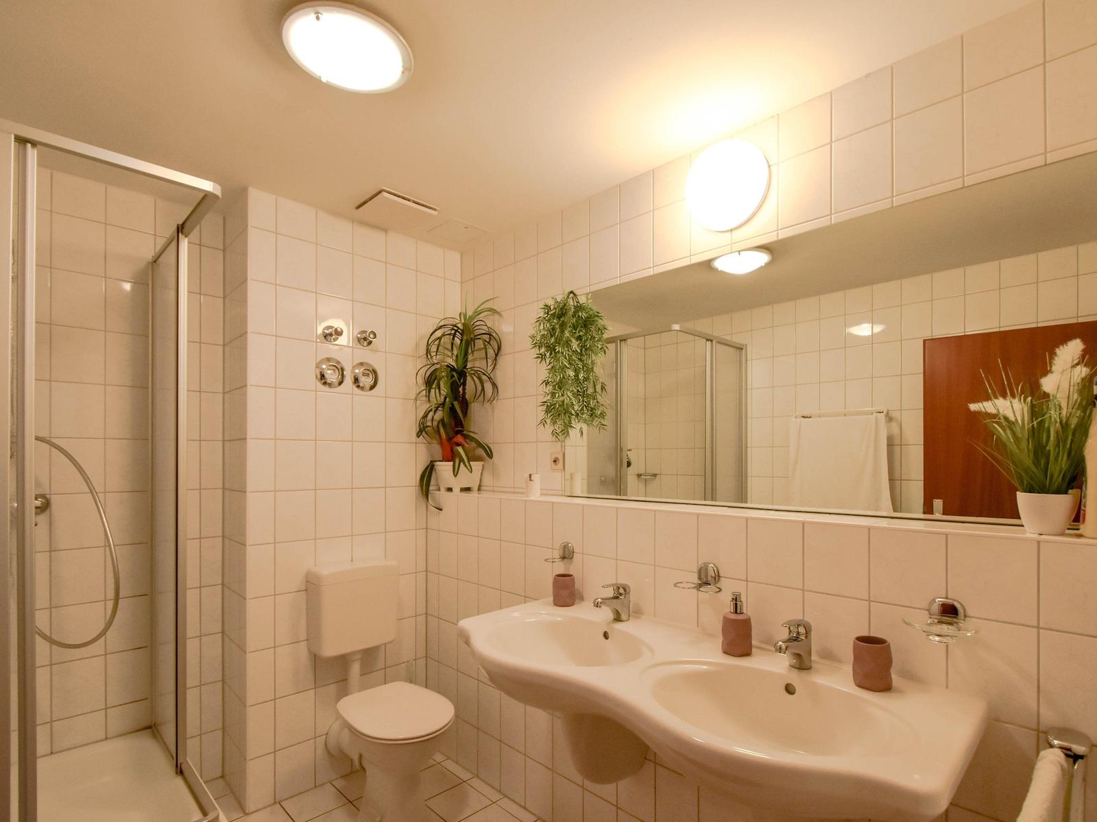 Badezimmer mit Dusche, Toilette und Doppelwaschbecken.