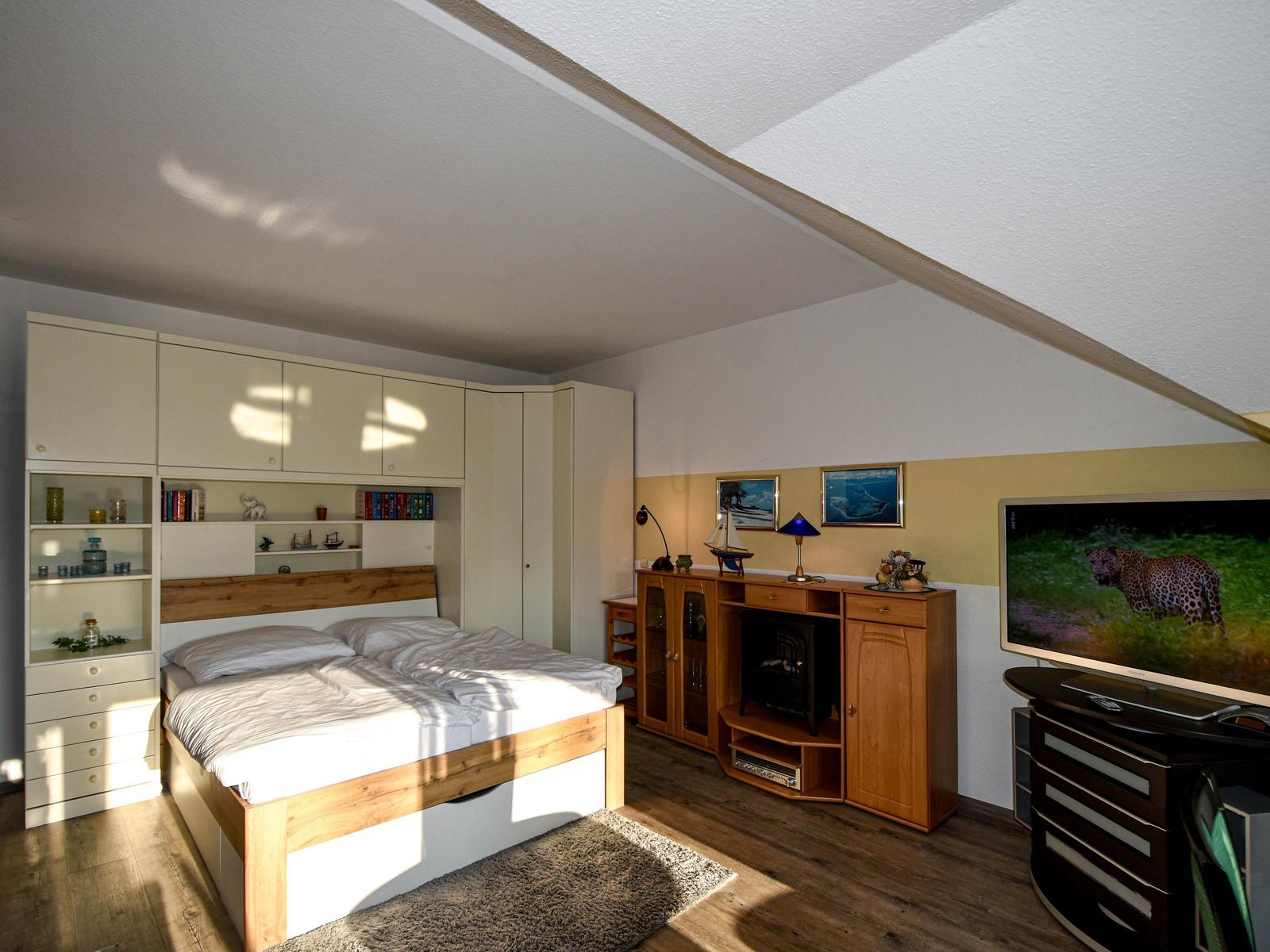 Schlafzimmer mit Bett, Schränken und Fernseher unter Dachschräge.