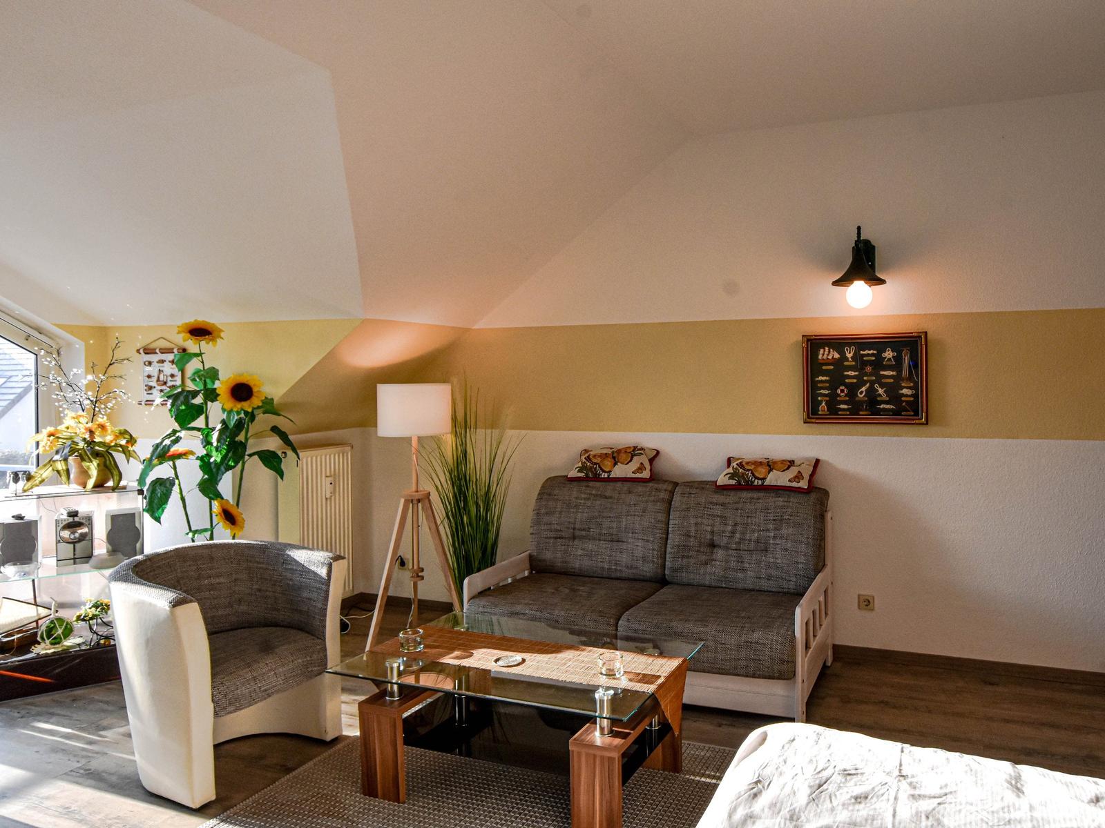 Wohnzimmer mit Sofa, Sessel und Glas-Tisch unter schrägen Decken.