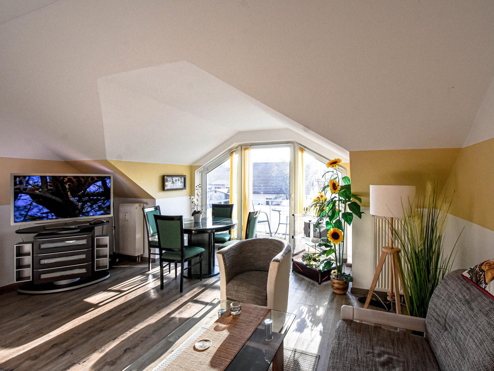 Wohn- und Essbereich mit TV, Sitzgelegenheiten und Balkonzugang.