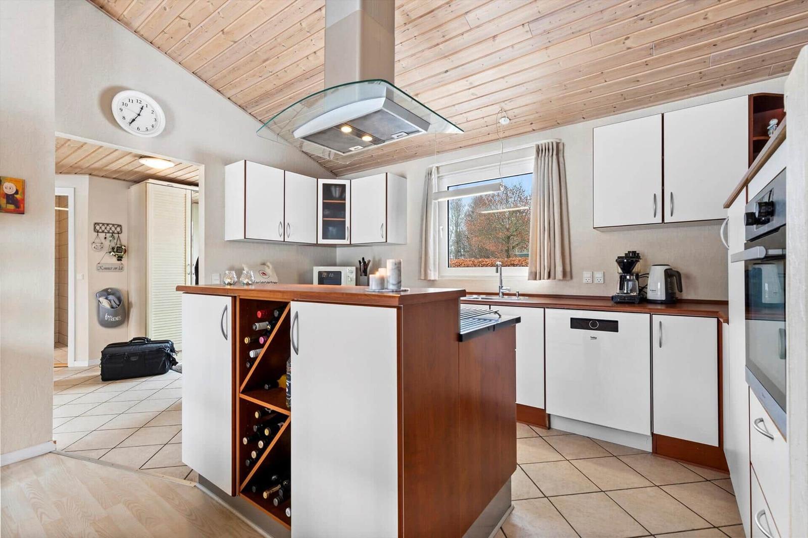 Kitchen with wooden ceiling, white cabinets, and central island with wine cellar.