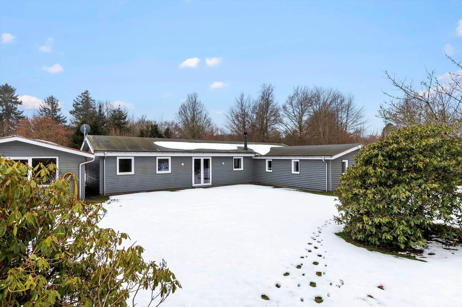 A gray house with a snow-covered yard and trees in the background.