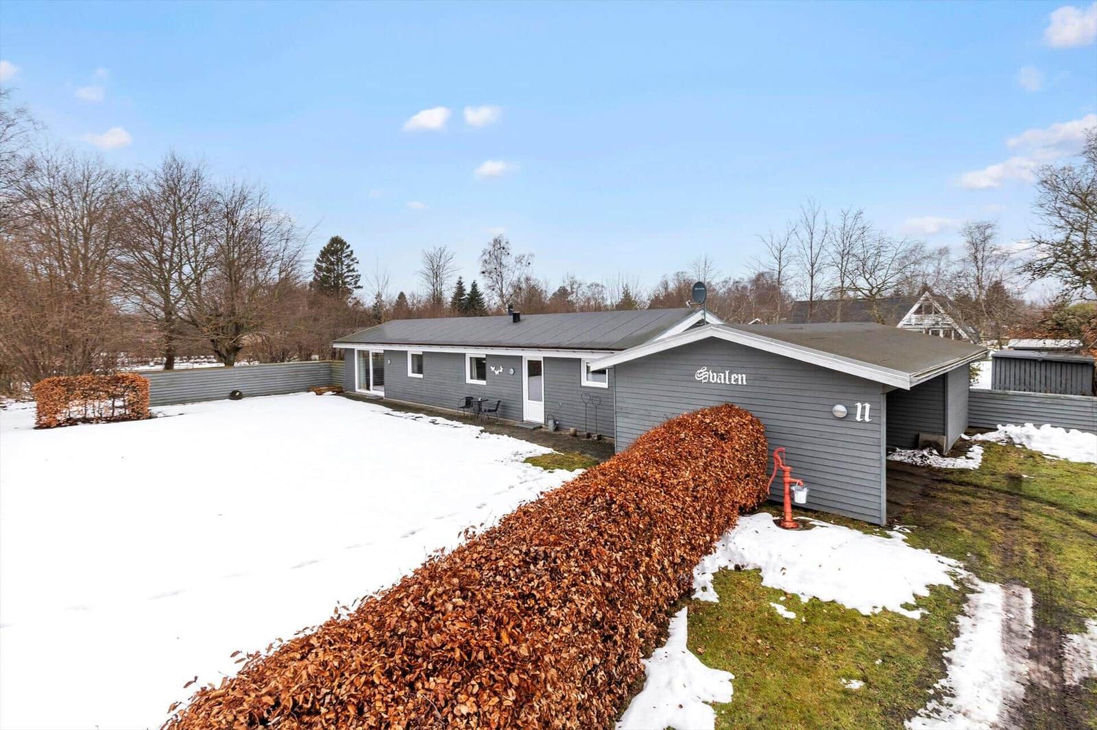 A gray vacation home with a snowy yard and hedge in the foreground.