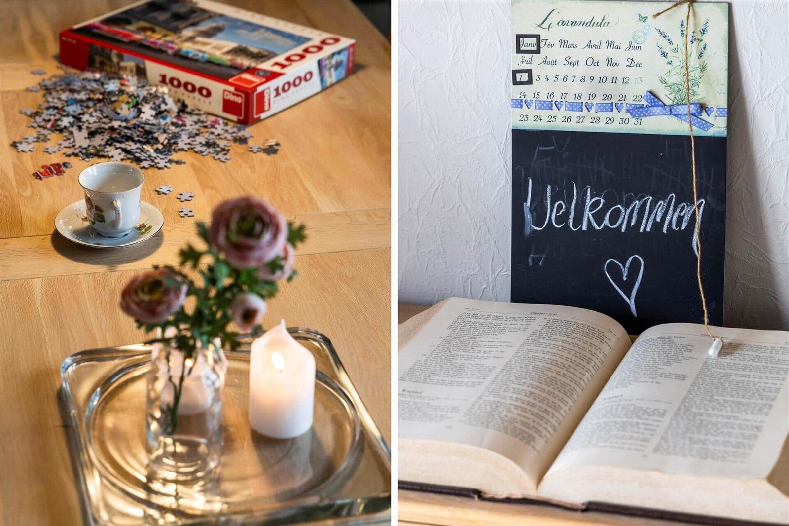 Table with puzzle, tea, flowers, and candle. Wall calendar and open book.