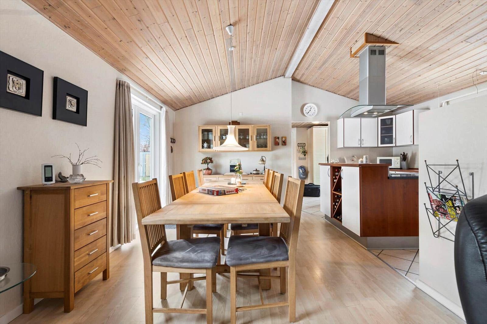 Dining area with wooden table, chairs, and kitchen with white cabinets.
