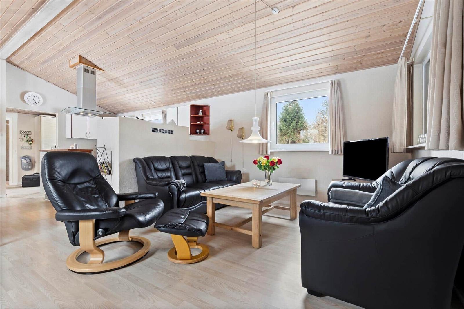 Living room with black leather furniture, wooden table, and wooden ceiling. Window with view of outdoor greenery.