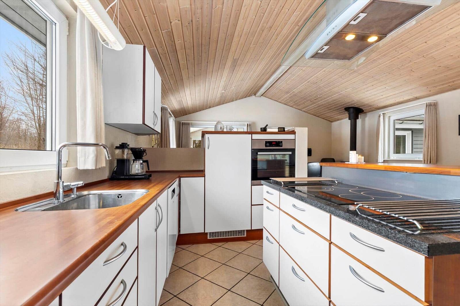 Kitchen with wooden ceiling, white cabinets, and stainless steel sink.