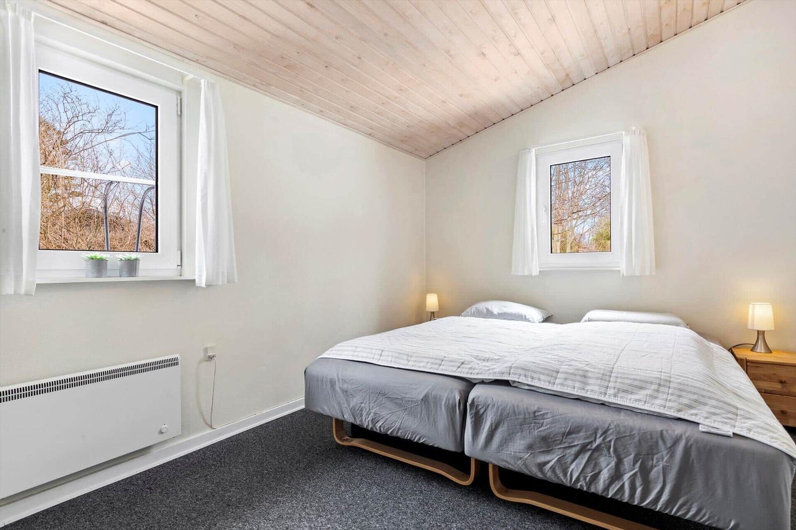 Bedroom with double bed, two windows, and wooden ceiling.