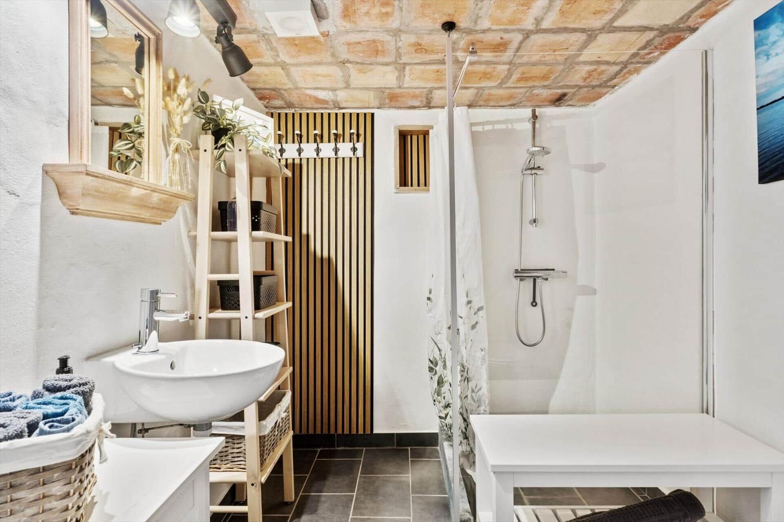 Bad mit Dusche, Waschbecken und Holzregal unter Ziegeldecke.