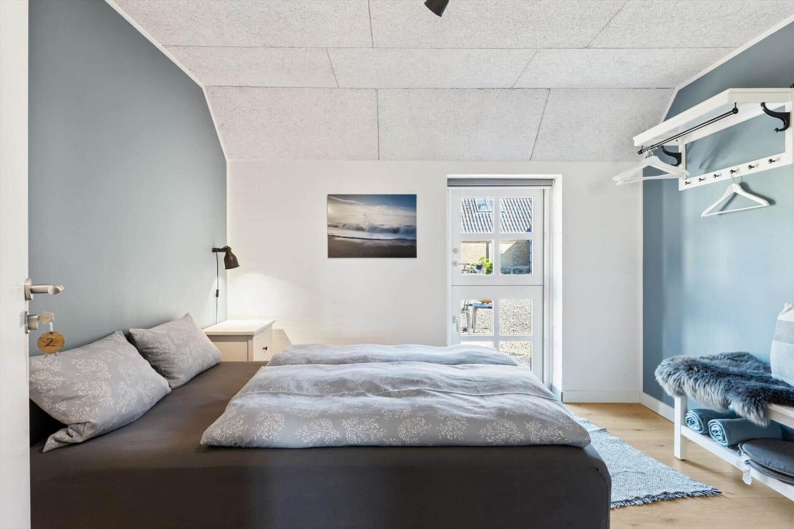 Schlafzimmer mit Bett, Kleiderständer und Tür zum Außenbereich.