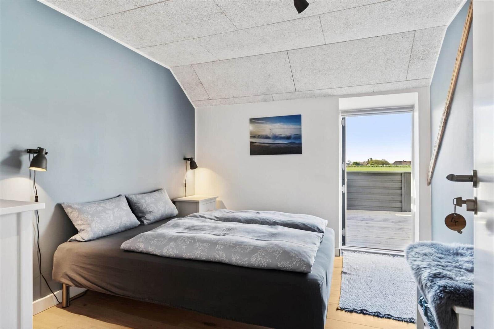 Schlafzimmer mit Bett, Decke, Tür zum Balkon und Wandbild.