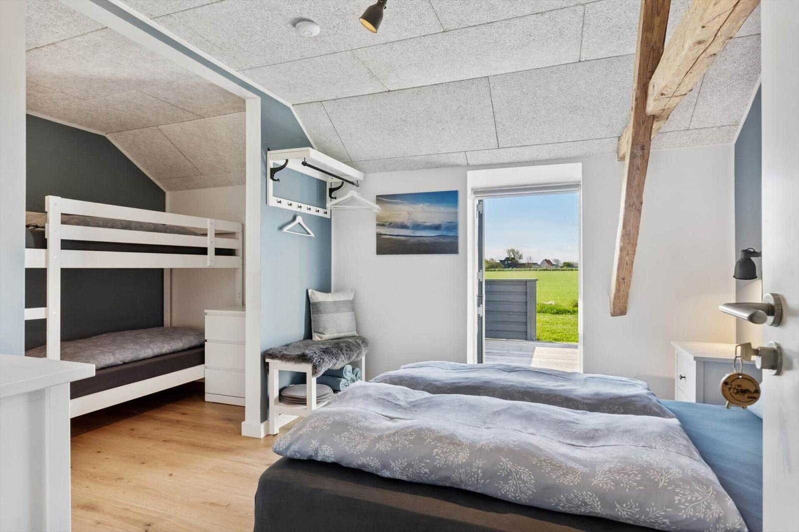 Schlafzimmer mit Doppelbett und Krippenbett. Tür führt auf Terrasse mit Blick auf Feld.