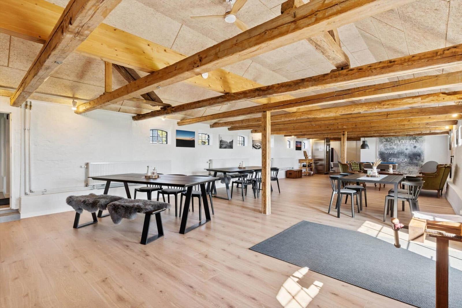 Großes Wohn- und Esszimmer mit Holzbalken, Tischen und Stühlen.