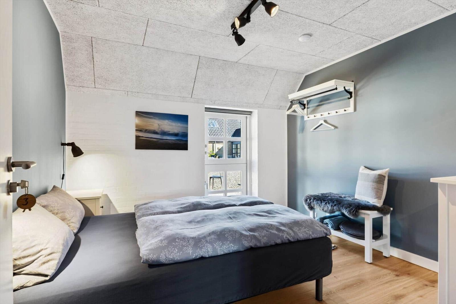 Schlafzimmer mit Bett, Kleiderständer und Fenster. Decke aus Betonplatten.
