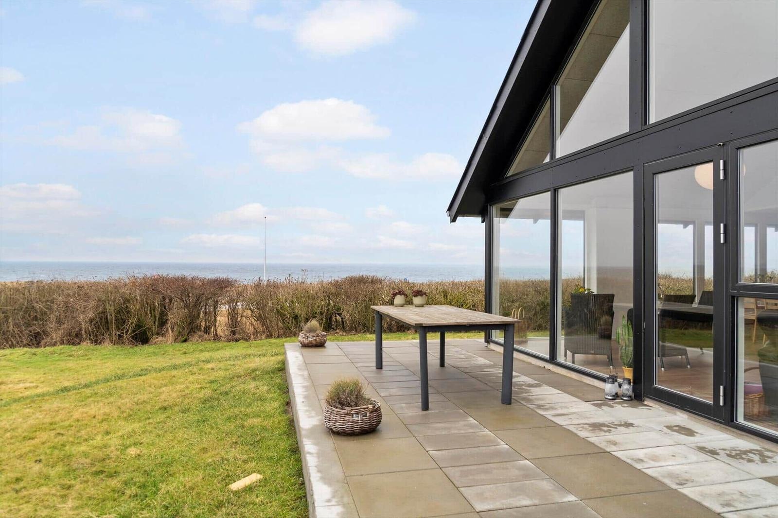 Terrasse mit Tisch und Blick aufs Meer. Glasfront führt ins Haus.