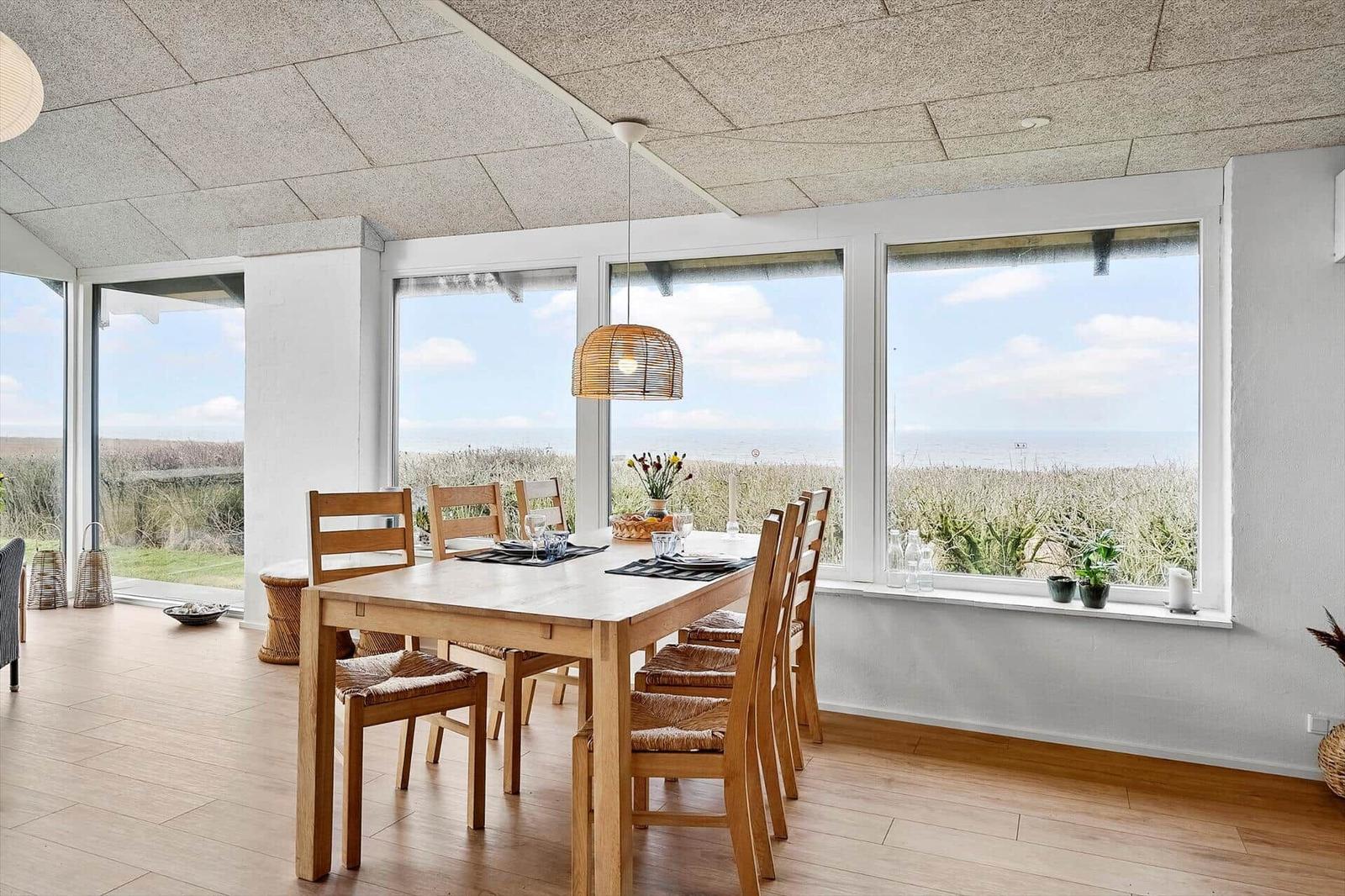 Esszimmer mit Tisch, Stühlen und Meerblick durch große Fenster.