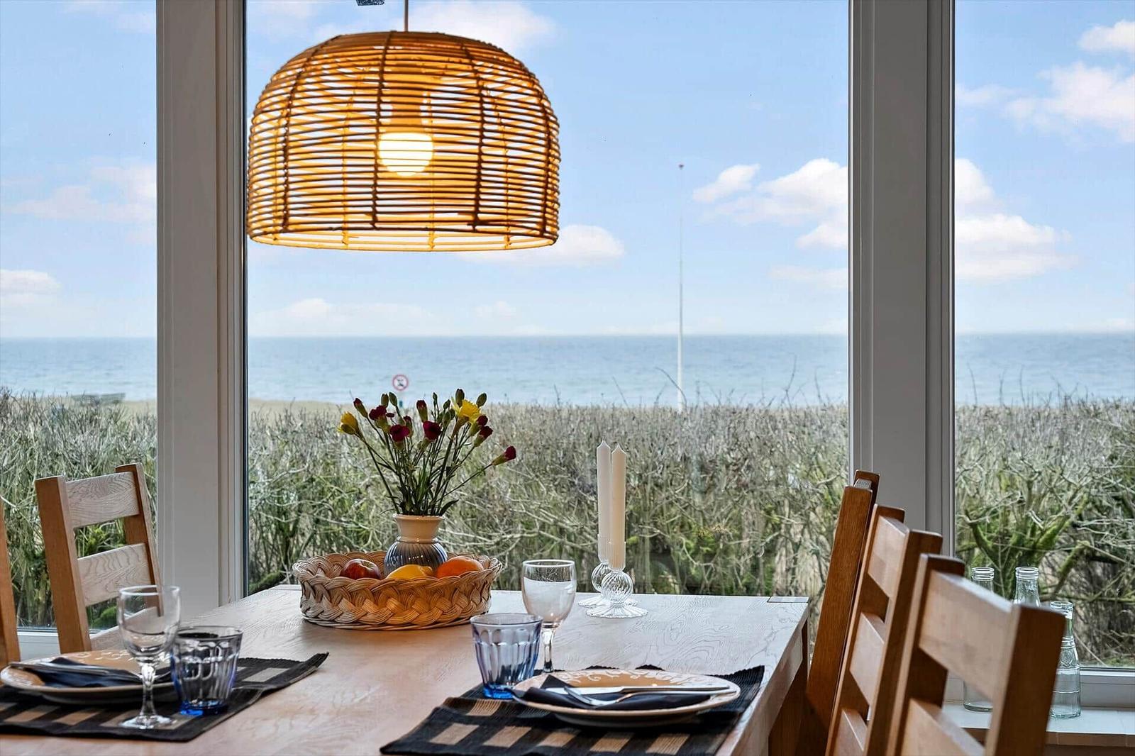 Esszimmer mit Meerblick, Holztisch, Stühle und Wickerlampe.