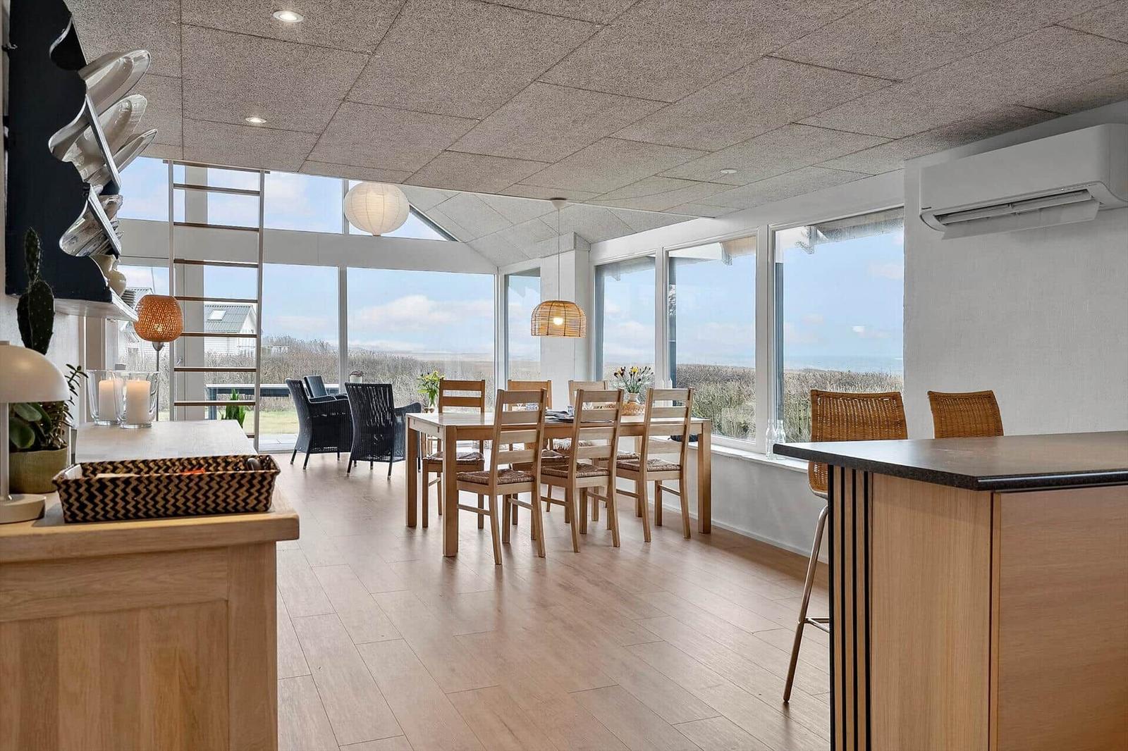 Großes Esszimmer mit Blick auf die Landschaft. Holztisch, Stühle, Fensterfront.